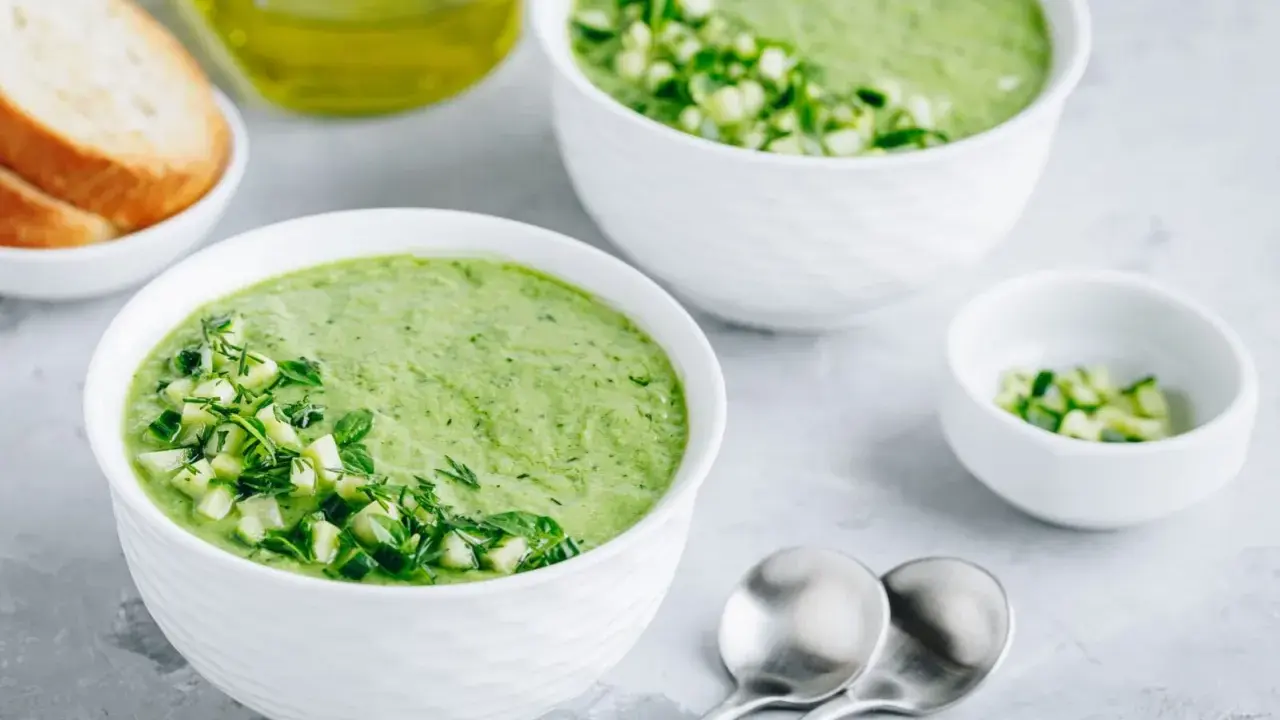 Deux bols de gaspacho concombre frais, garni de dés de concombre et d'herbes. Du pain grillé et de l'huile d'olive à proximité.