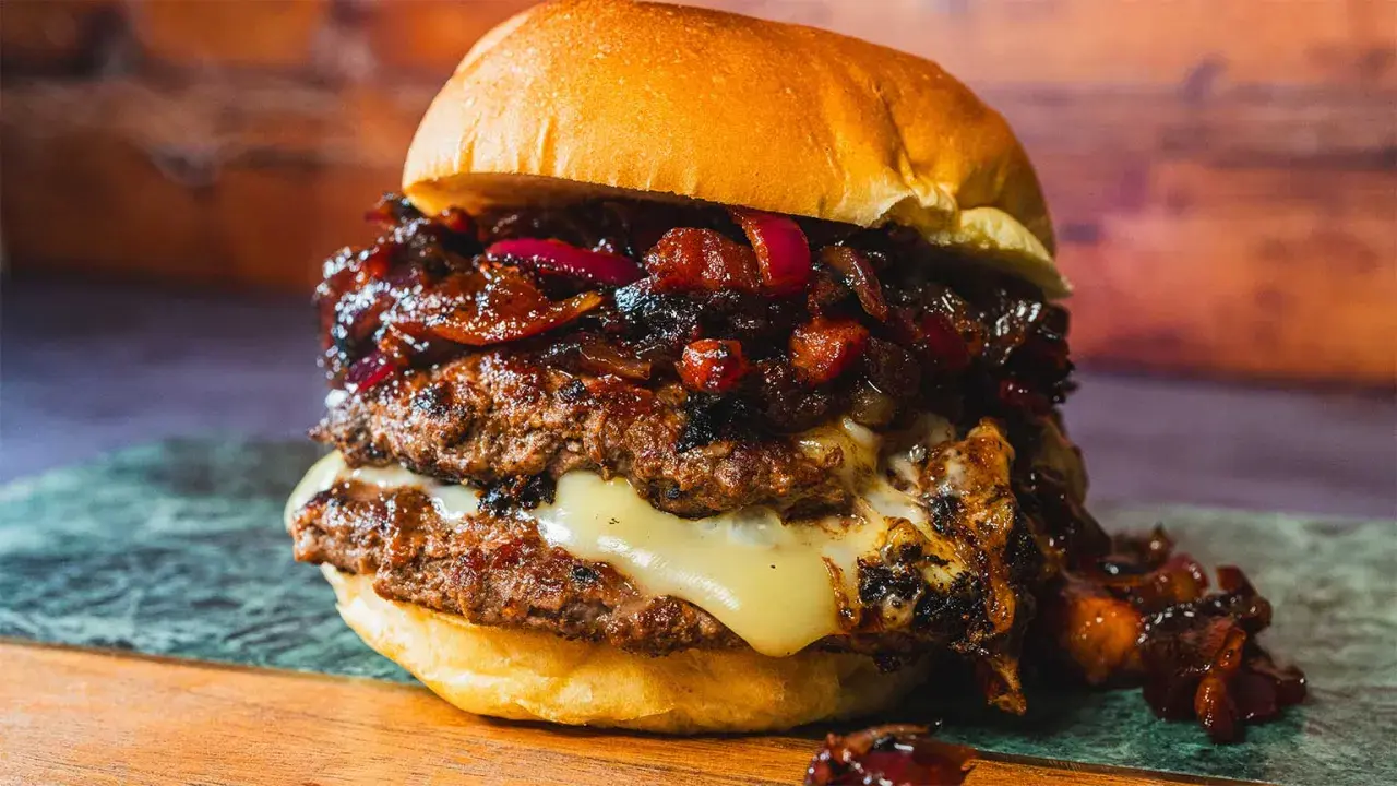 Saftiger Burger mit doppeltem Patty, geschmolzenem Käse und einer süß-salzigen Bacon Jam-Schicht, garniert mit roten Zwiebeln.