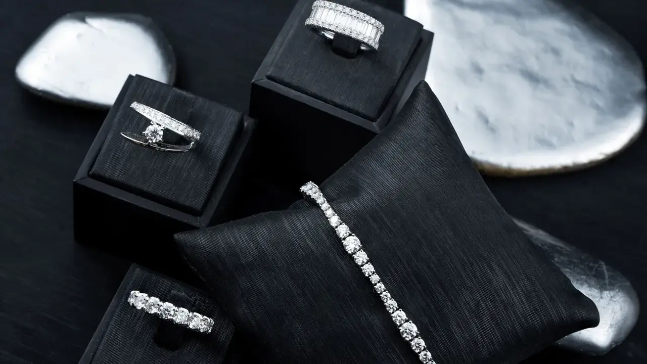 Gioielli scintillanti, anelli e bracciali con diamanti, esposti su supporti neri e pietre levigate.