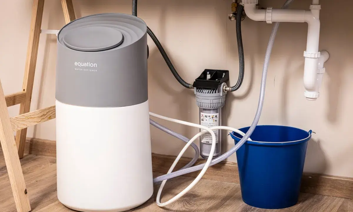Instalación de descalcificador Equation bajo el fregadero, con filtro y cubo azul para recoger agua.