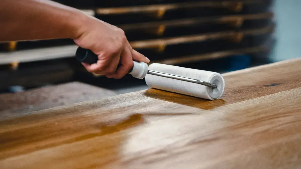 Main d'artisan appliquant une couche de vernis sur une table en bois avec un rouleau, pour la protéger et la sublimer.