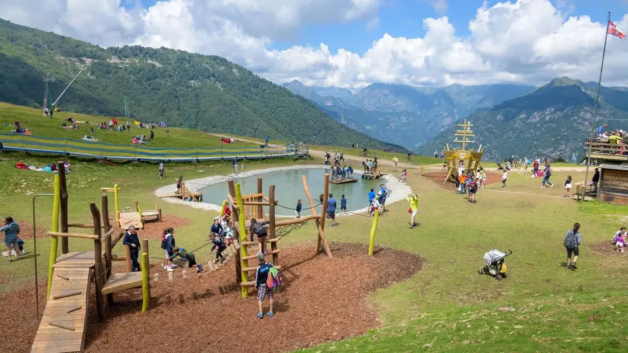 Un parco giochi in montagna con un laghetto, un galeone e tante famiglie che si divertono. Perfetto per le vacanze in montagna con bambini.