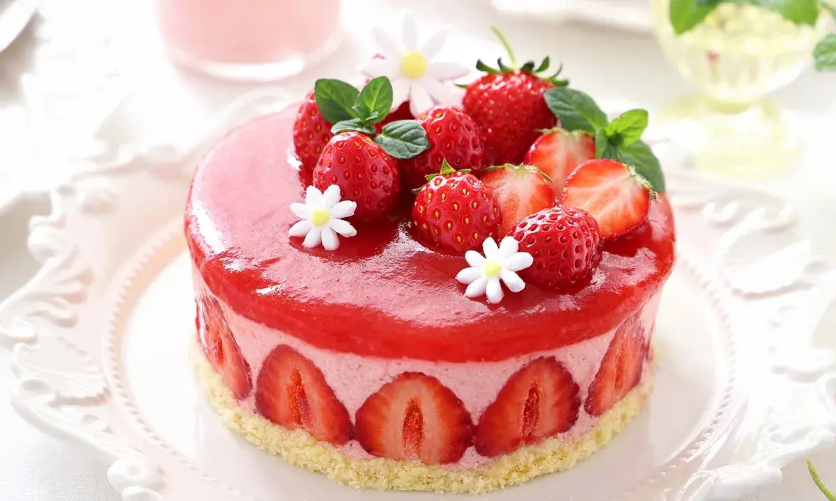 Deliziosa bavarese alle fragole, decorata con fragole fresche, menta e fiorellini bianchi, su una base croccante.