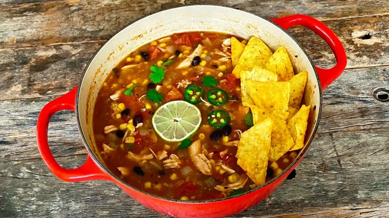 Prawdziwa zupa meksykańska w czerwonym garnku, pełna kurczaka, fasoli, kukurydzy, z limonką i jalapeño. Chrupiące nachos na wierzchu.
