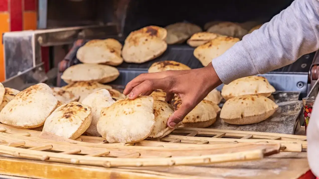 En hand tar färskt, fluffigt bröd från en ugn. Detta är en del av den autentiska egyptiska maten, perfekt för att doppa i läckra röror.