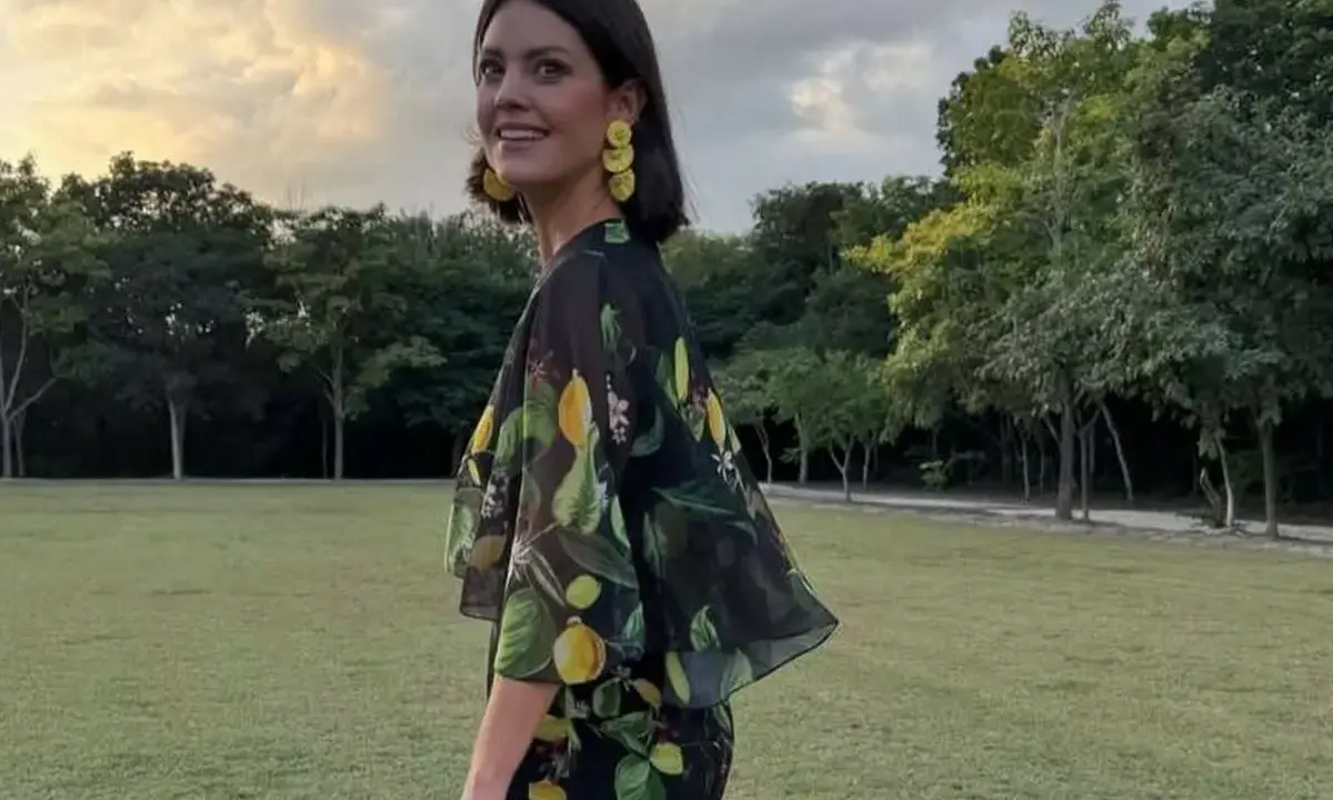 Isabelle Junot sonríe con un vestido estampado de limones, luciendo pendientes amarillos y un sombrero de paja en un día soleado.