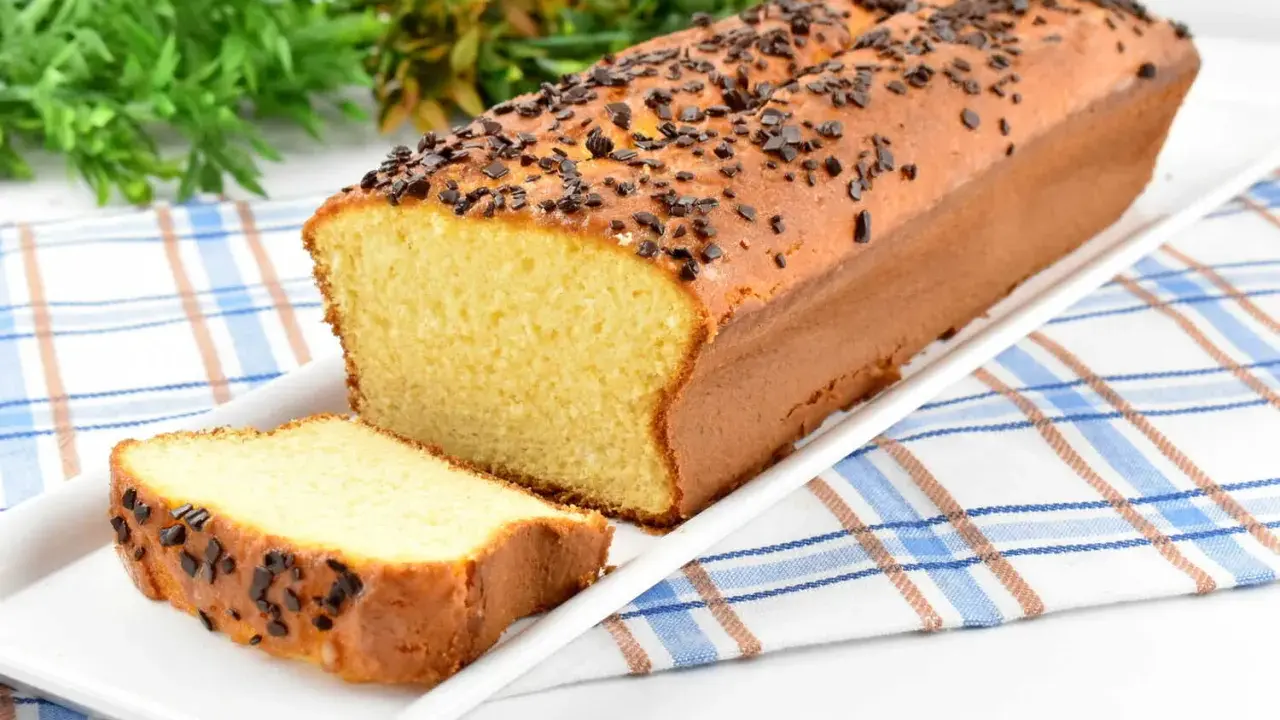 Puszysta babka z adwokatem, posypana czekoladową posypką, na białej paterze. Obok leży kromka ciasta.