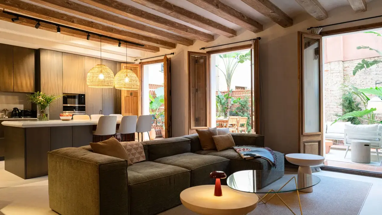 Salón moderno con vigas de madera vistas, sofá modular, cocina integrada y acceso a patio. Ideal para poner falso techo y unificar espacios.