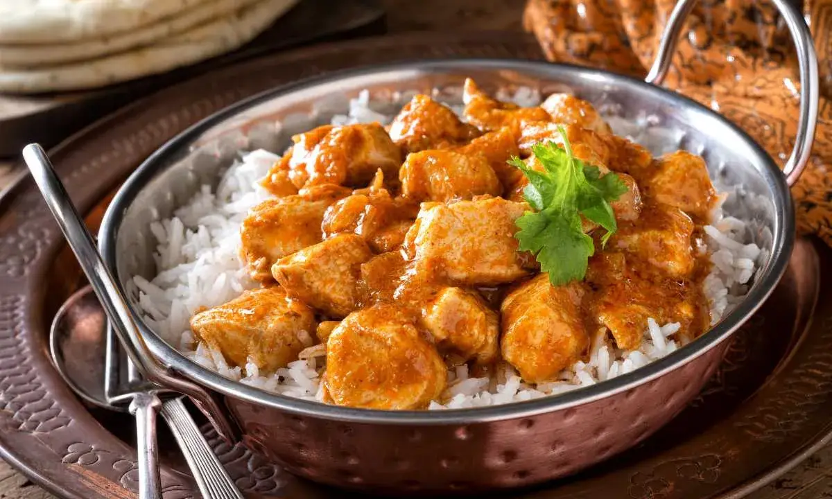 Un delicioso pollo al curry, un plato que evoca los sabores de la India, servido sobre arroz blanco en un cuenco de cobre.