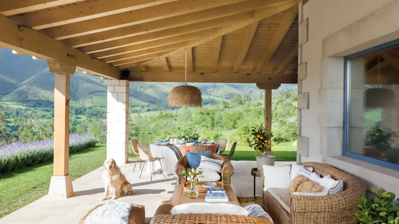 Ideas para como decorar porche de entrada: muebles de mimbre, mesa de comedor, un perro y vistas espectaculares.
