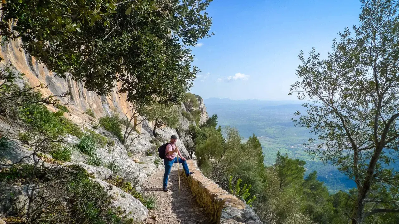 Mann mit Wanderstock und Rucksack genießt die Aussicht auf Mallorca. Ein toller Tag zum Wandern auf Mallorca!