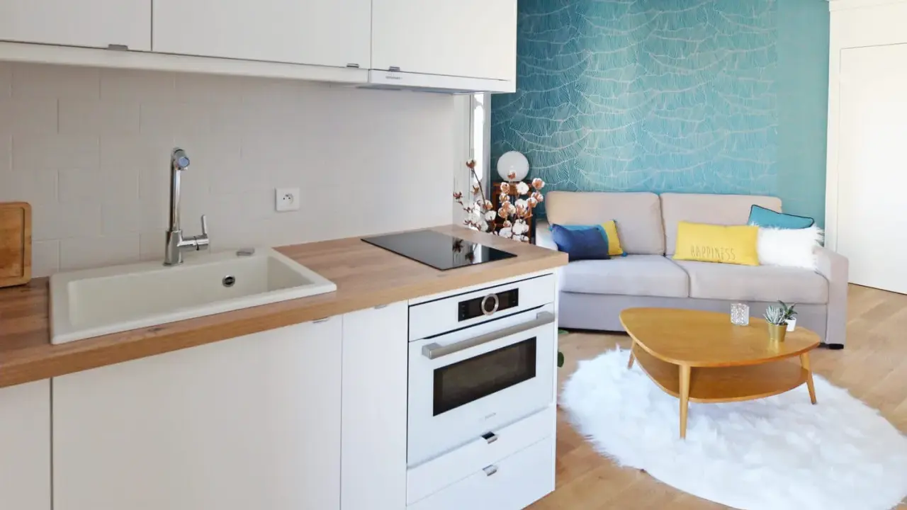 Aménagement petite cuisine moderne avec évier, plaque induction, four et salon cosy avec canapé bleu et jaune.