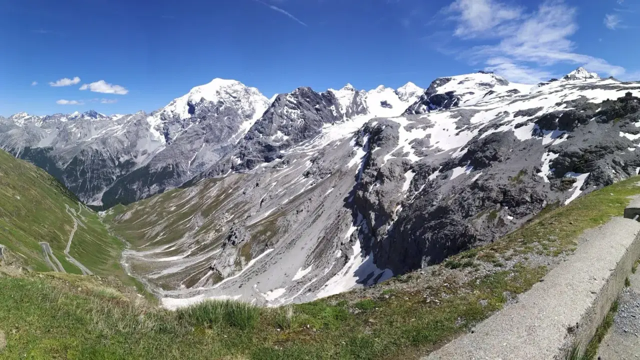 Panoramica mozzafiato dei fotografi sui tornanti dello Stelvio, con vette innevate e un cielo azzurro intenso.