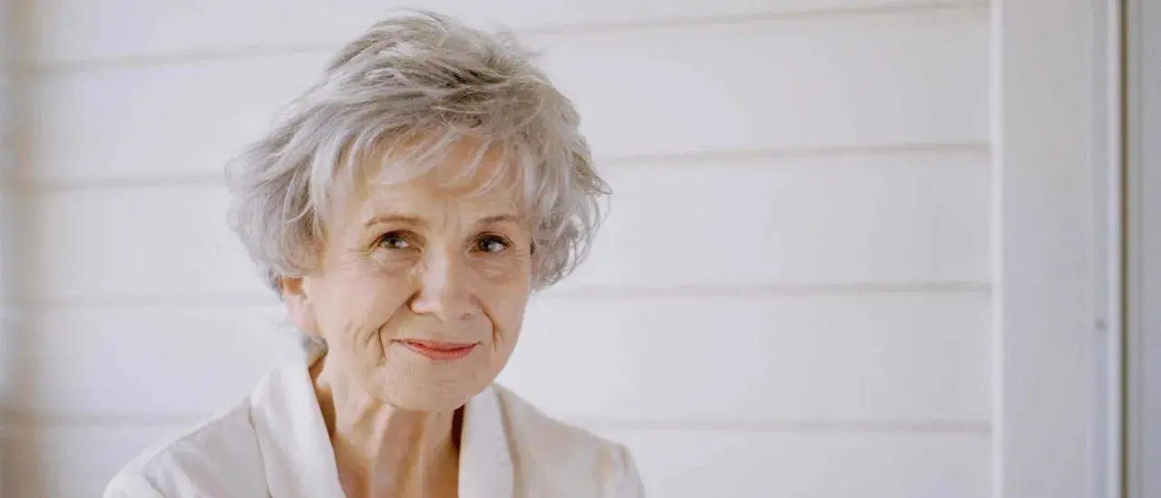 Ritratto di Alice Munro, con capelli grigi spettinati e un sorriso gentile.