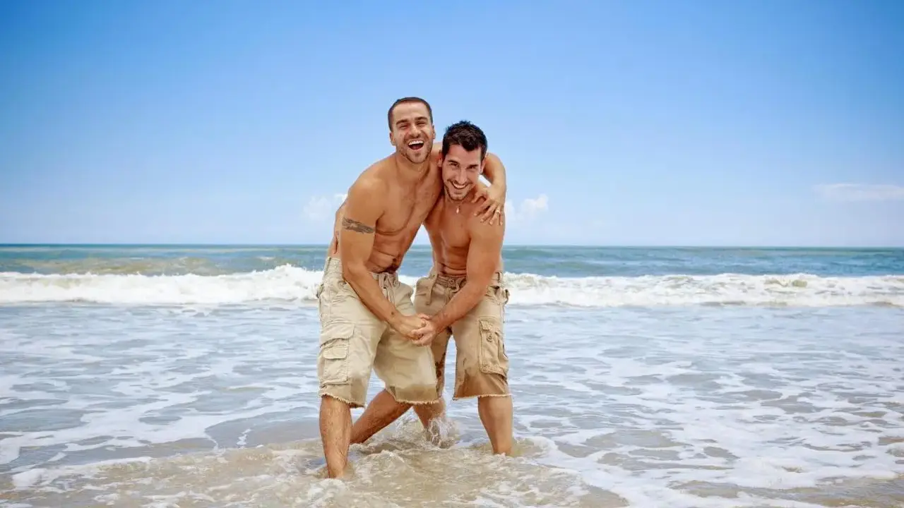 Two men laughing and embracing in the shallow waves of the Torremolinos gay beach.