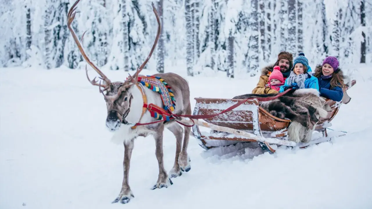 Familie im Rentierschlitten im verschneiten Wald, ein magischer Ausflug im Weihnachtsmann-Dorf Finnland.