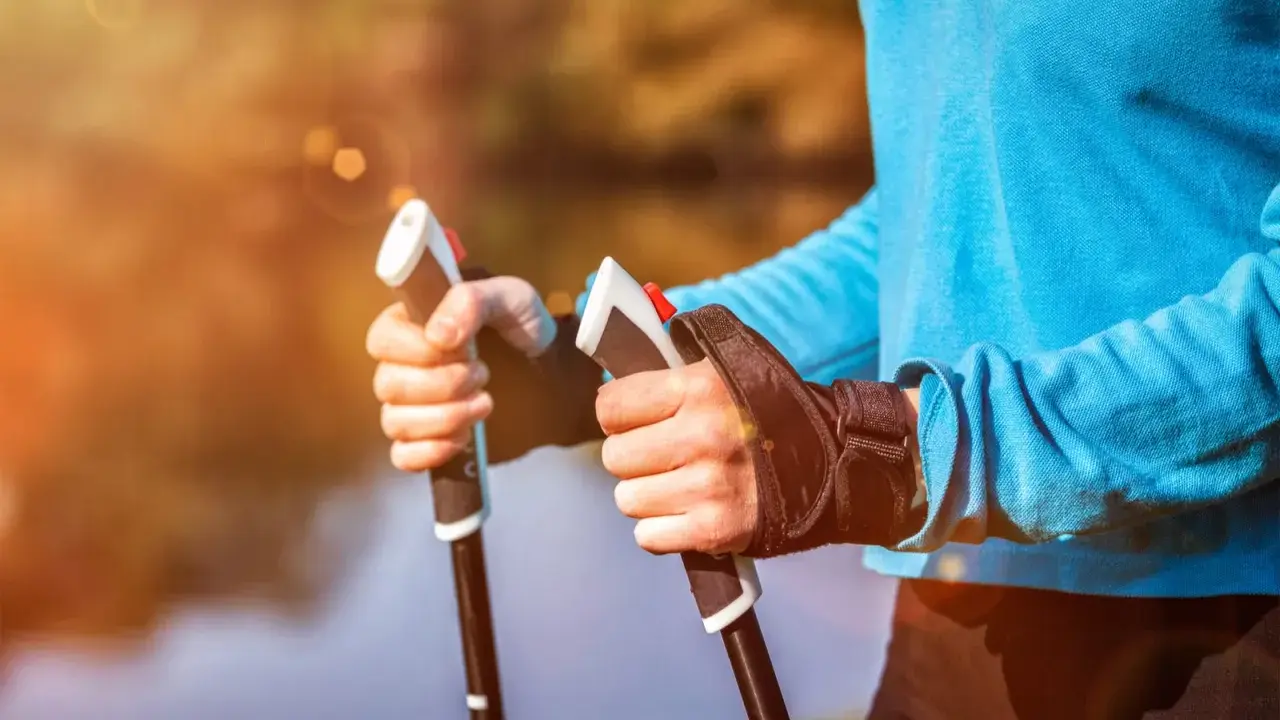 Radość z aktywnego życia po przeszczepie nerki. Dłonie trzymające kije do nordic walking na tle jesiennego krajobrazu.