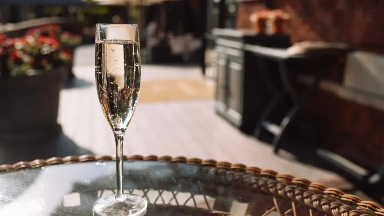 Ein Glas Sekt auf einem Tisch im Freien. Auch wenn Sekt kein Verfallsdatum hat, sollte er frisch genossen werden.