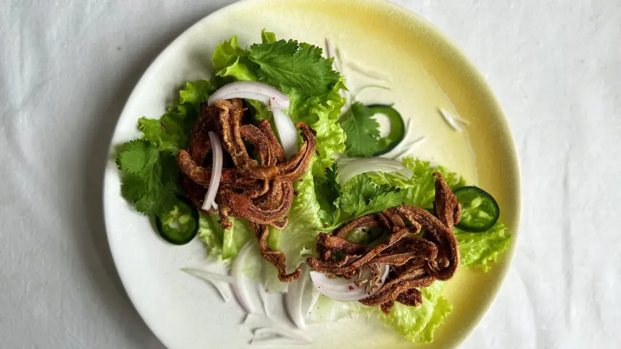 Crujiente oreja de cerdo frita servida sobre lechuga con cebolla morada, cilantro y jalapeño.