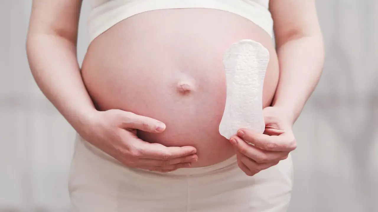 Ciężarna kobieta trzyma podpaskę, sugerując pytanie: czy w okres można zajść w ciążę?