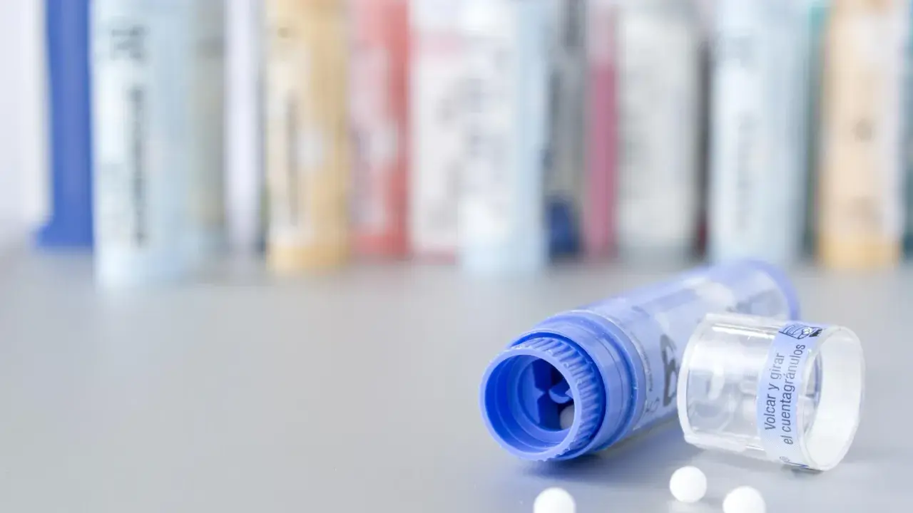 Flacons de granules homéopathiques, certains en arrière-plan floutés. Un tube bleu ouvert laisse échapper quelques billes blanches. Une solution naturelle pour la dermite séborrhéique, comme une huile essentielle, pourrait être contenue dans ces remèdes.