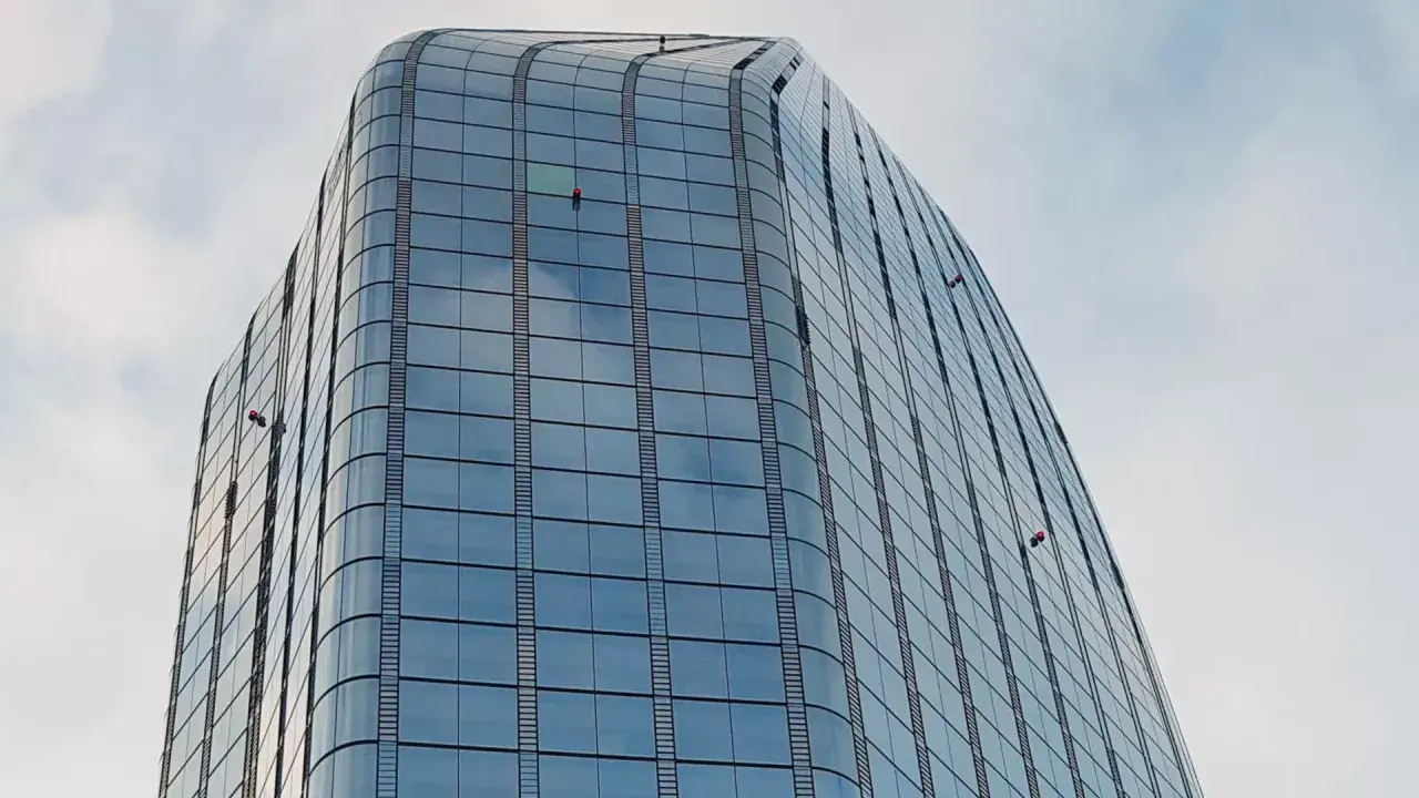 Trabajadores en altura limpian ventanas de edificio moderno. Sikaflex para que sirve: sellar y unir, asegurando la integridad de estas estructuras.