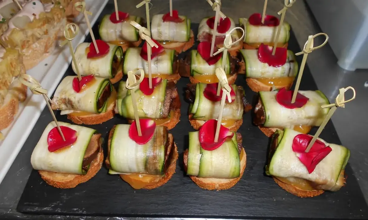 Variedad de tipos de pinchos con calabacín enrollado, pétalos rojos y palillos de bambú.