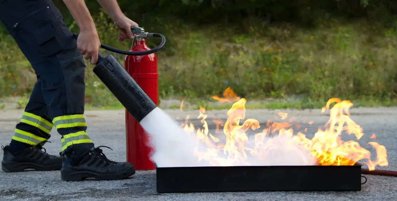 Person i skyddskläder släcker eld med brandsläckare. Praktisk brand utbildning för säkerhet.