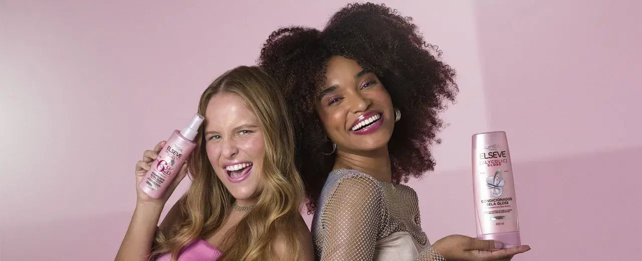 Dos mujeres sonríen, una con pelo liso y otra con pelo esponja, ambas sostienen productos Elseve para un brillo espectacular.