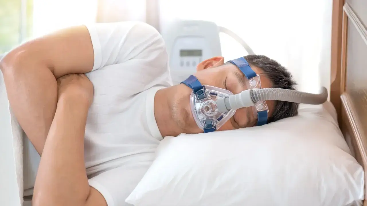 Mężczyzna śpi z maską CPAP, która pomaga mu oddychać podczas snu, łagodząc objawy bezdechu nocnego.
