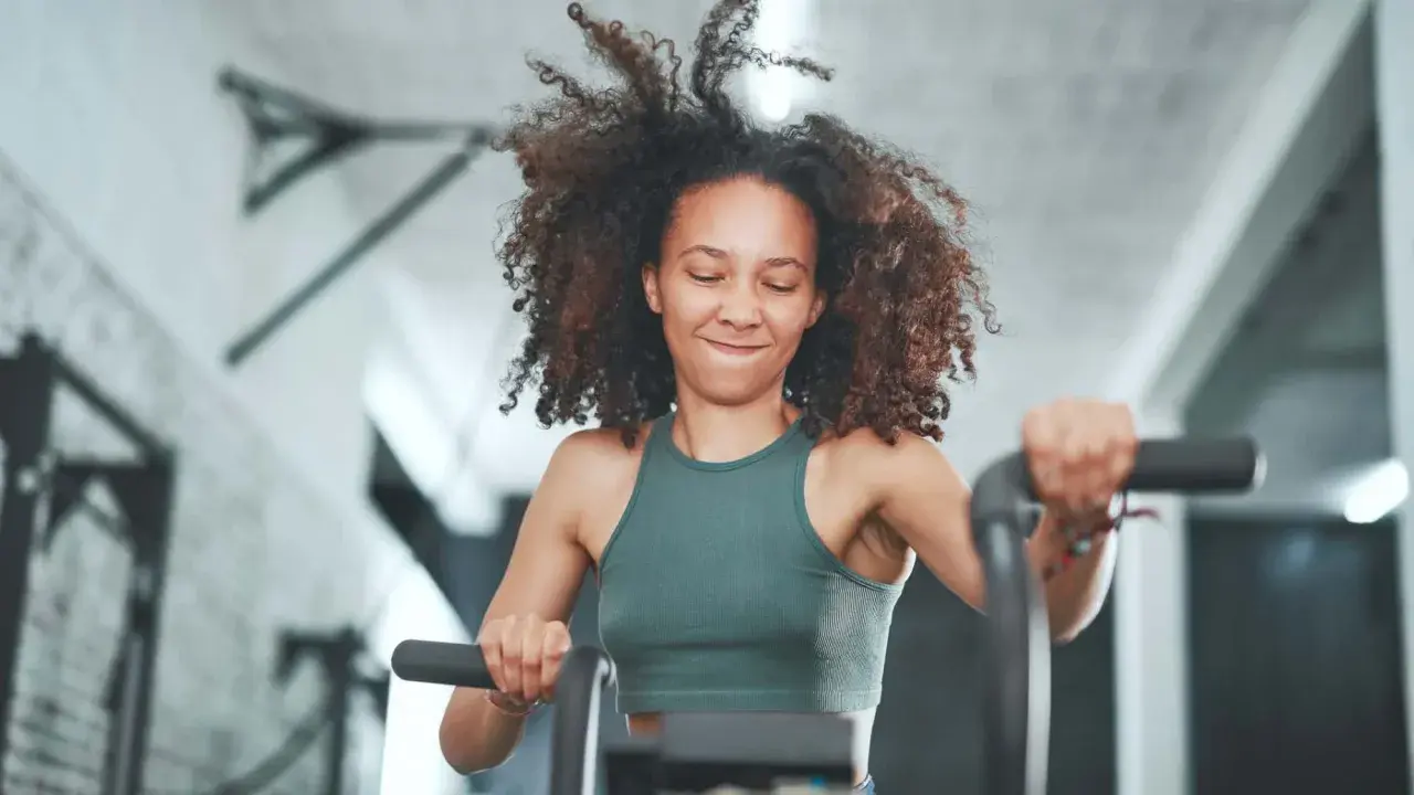 Frau mit lockigem Haar trainiert intensiv auf einem Fahrrad. Sie gibt alles, was ist HIIT – High Intensity Interval Training.