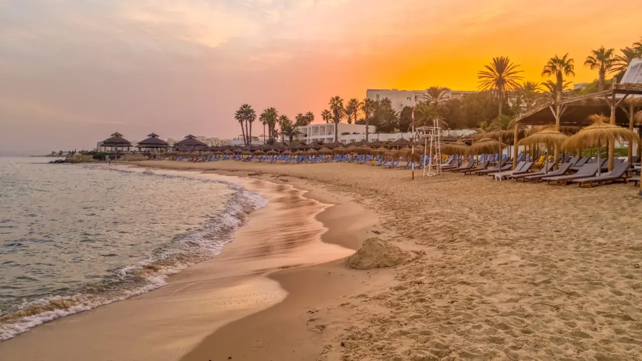 Strand in Tunesien im Oktober: Sanfte Wellen, Palmen und Liegestühle unter einem warmen Sonnenuntergang. Perfektes Wetter für einen entspannten Urlaub.