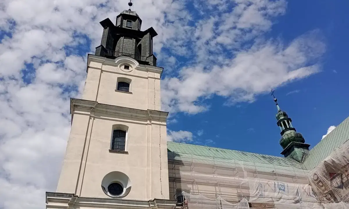 Wieża kościoła w Gidlach pod błękitnym niebem z chmurami. Widać fragment dachu w rusztowaniach.
