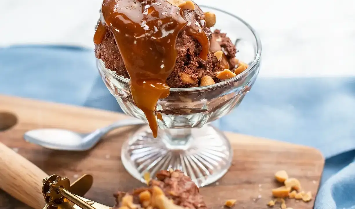 En skål med chokladglass, toppad med kolasås och nötter. Perfekt för ett chokladglass recept!