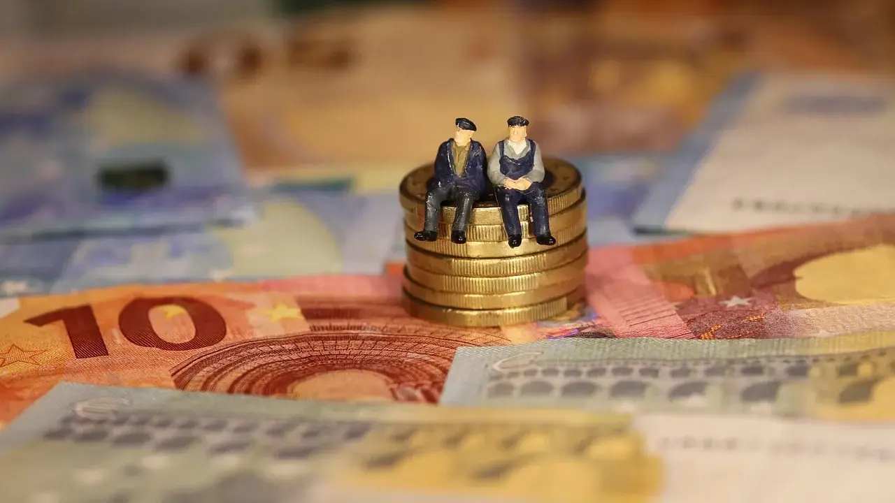 Dos figuritas sentadas en monedas de oro sobre billetes de euros. Reflexionan: como puedo cotizar los años que me faltan.