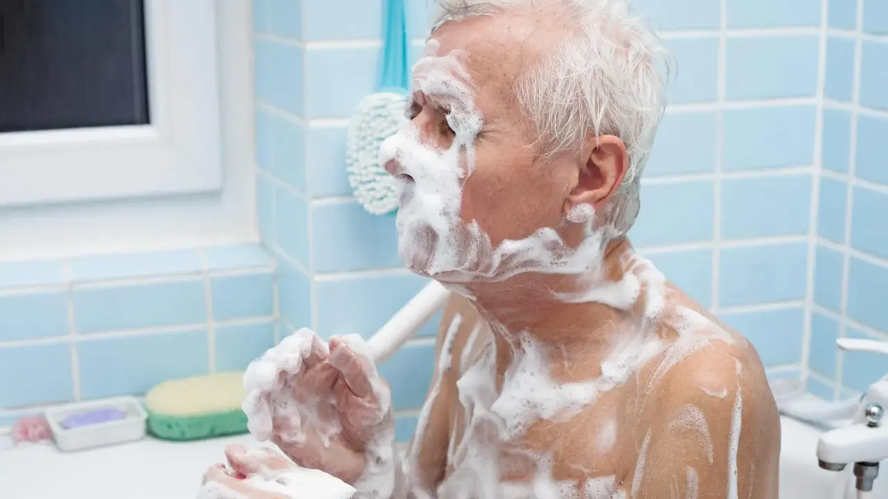 Un anziano con Alzheimer, coperto di schiuma, si lava. Un gesto di cura per convincerlo a lavarsi.
