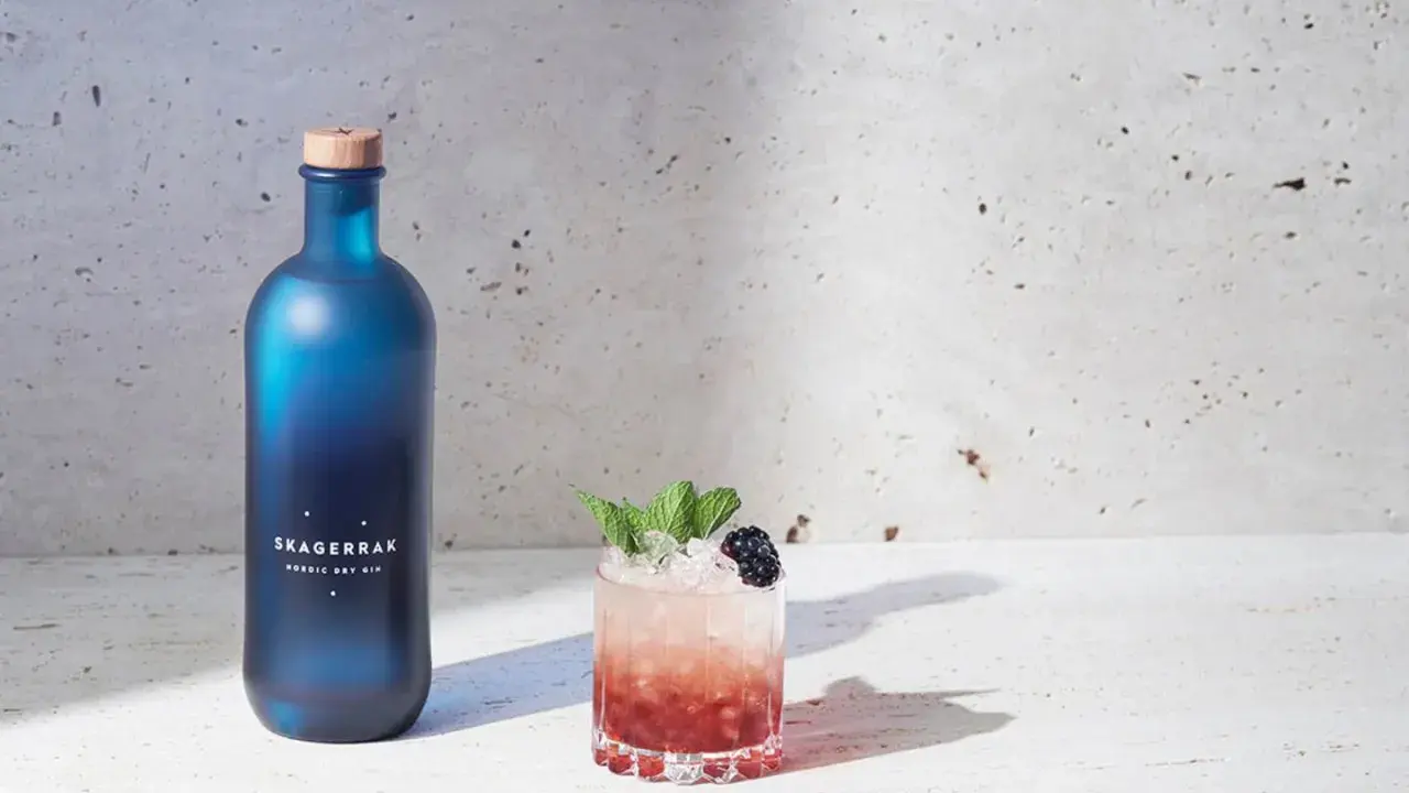 En blå flaska Skagerrak Nordic Dry Gin bredvid en läcker bramble drink med björnbär och mynta.