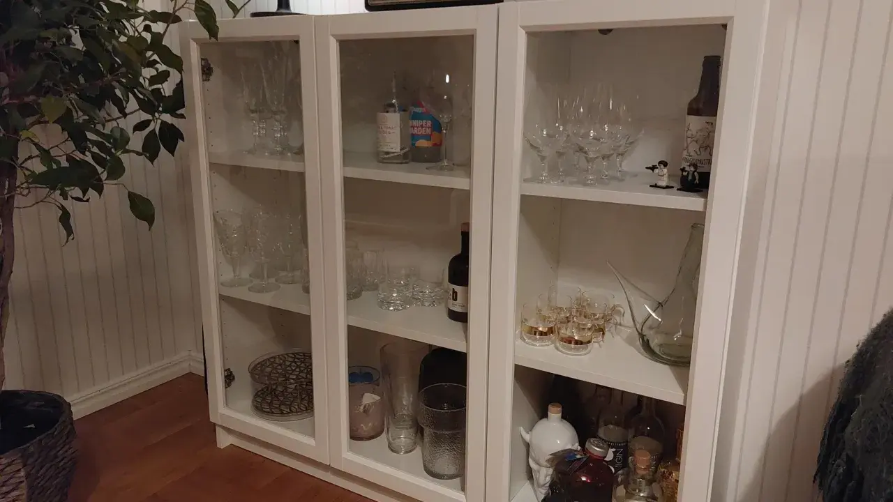 Ett DIY-projekt med ett vitt Billy vitrinskåp fyllt med glas, flaskor och dekorationer.