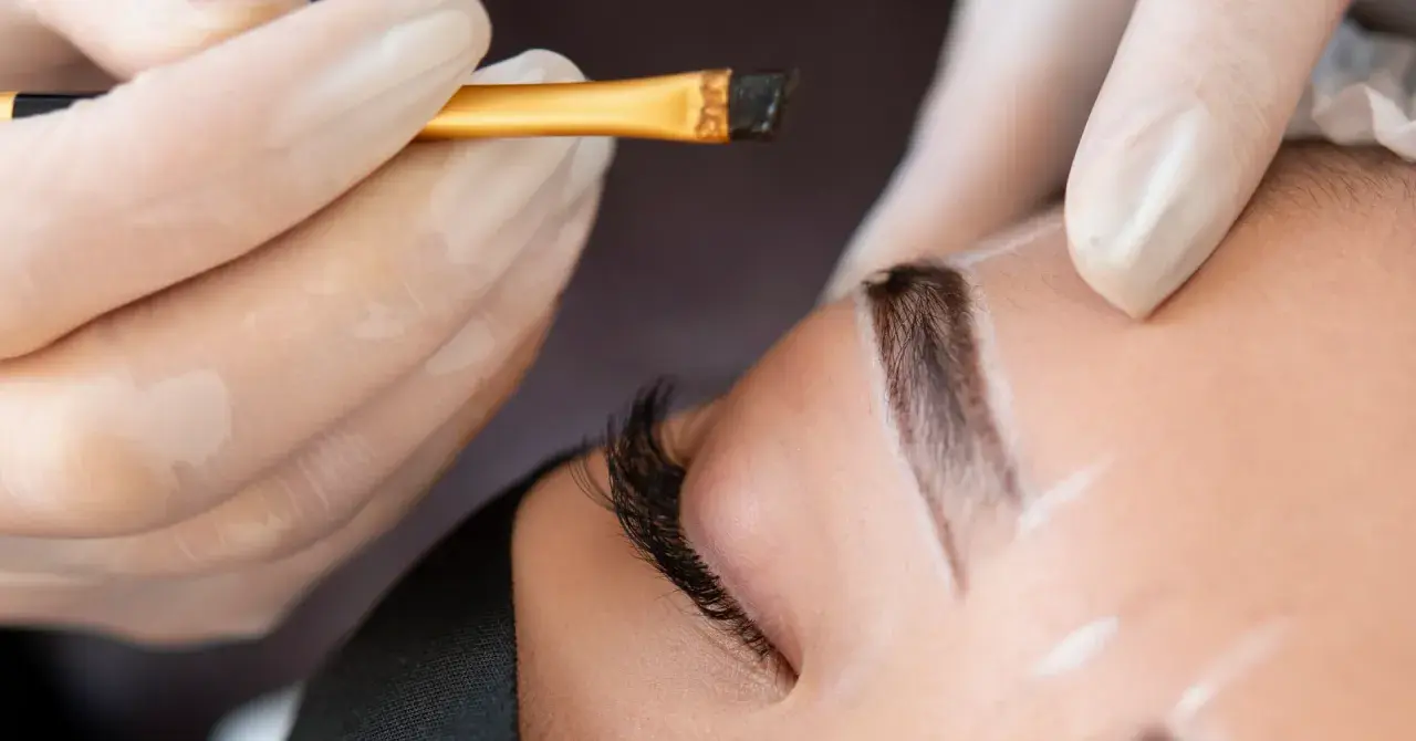 Application d'une teinture sourcils en institut. Un pinceau fin dépose la couleur sur un sourcil soigneusement dessiné.