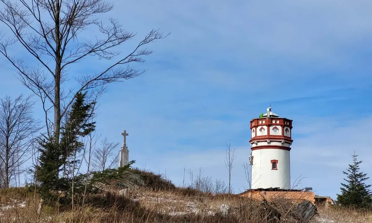 Wieża widokowa i krzyż na wzgórzu w Górach Opawskich. Szlaki prowadzą przez suchą trawę i nagie drzewa.