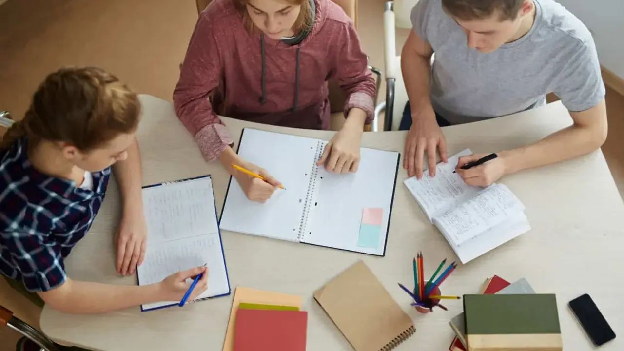 Trzech studentów pracuje nad pracą licencjacką, analizując metody badawcze.