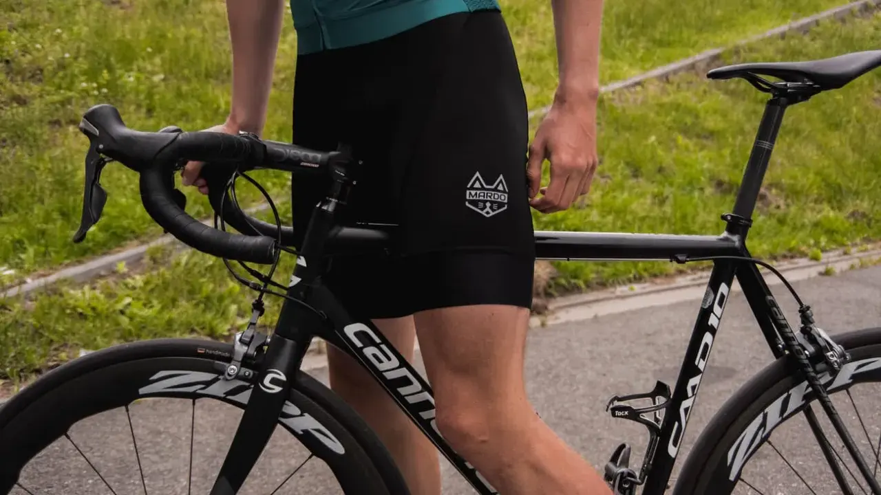 Kolarz w czarnych spodenkach i zielonej koszulce przygotowuje się do treningu kolarskiego. Rower szosowy Cannondale czeka na jazdę.