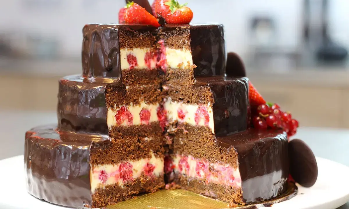 Gâteau à trois étages au chocolat et aux framboises, parfait pour une recette gâteau anniversaire facile. Décoré de fruits rouges et de chocolat.