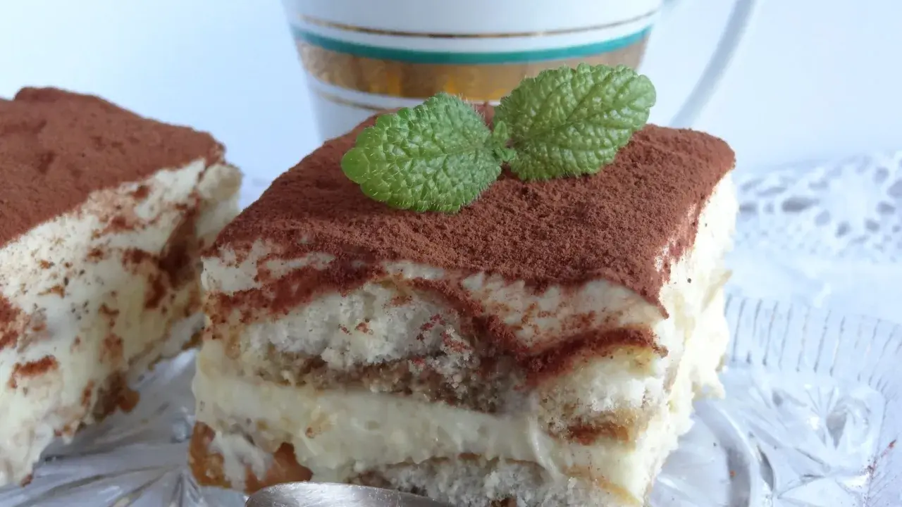 Pyszne tiramisu bezglutenowe, posypane kakao i udekorowane listkiem mięty, czeka na łyżeczkę.