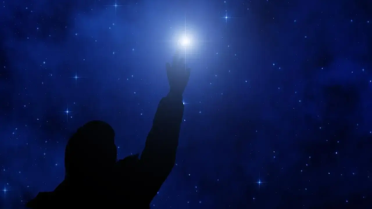 Sylwetka człowieka sięga ku jasnej gwieździe polarnej na tle nocnego, gwiaździstego nieba.