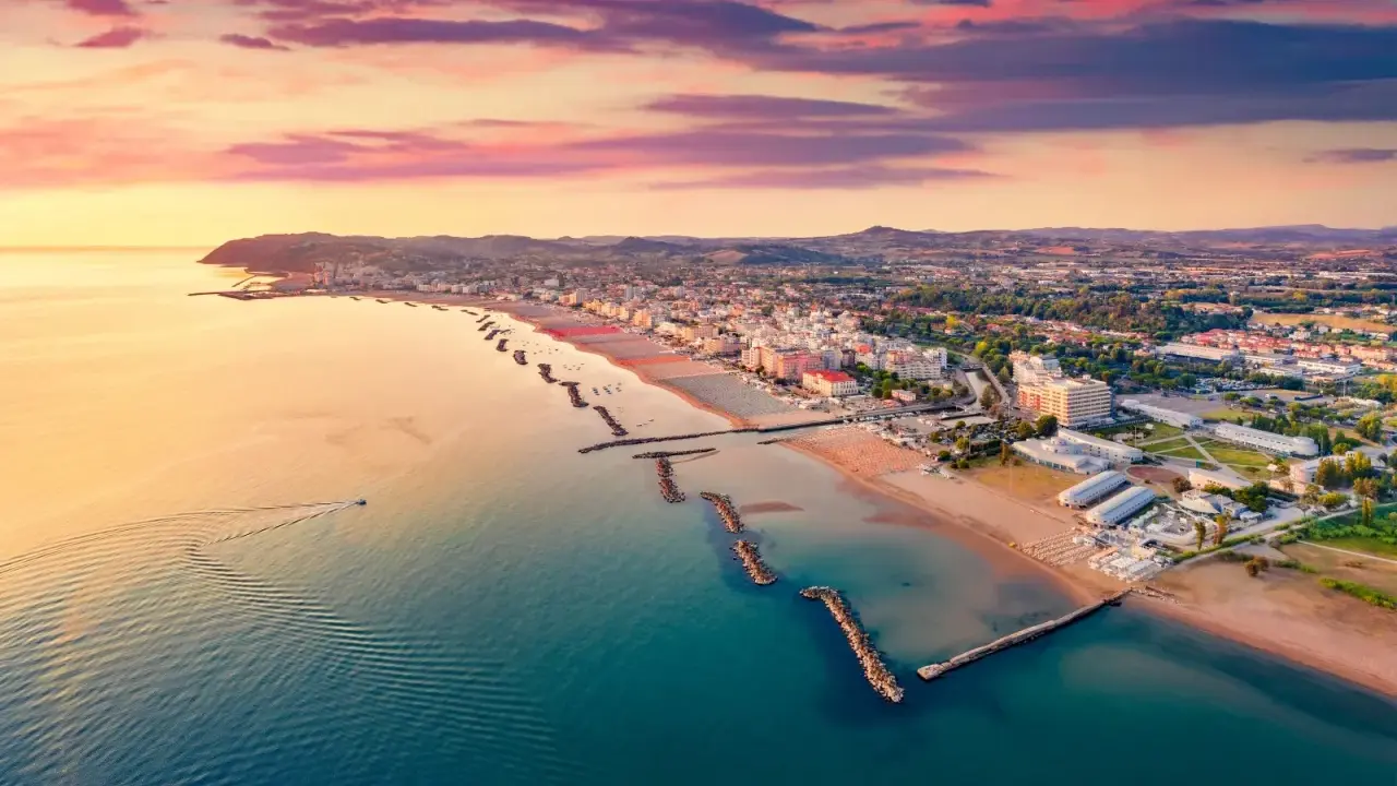 Alba rosa sul cattolica mare, con la costa e le colline sullo sfondo. Una barca solca le acque calme.