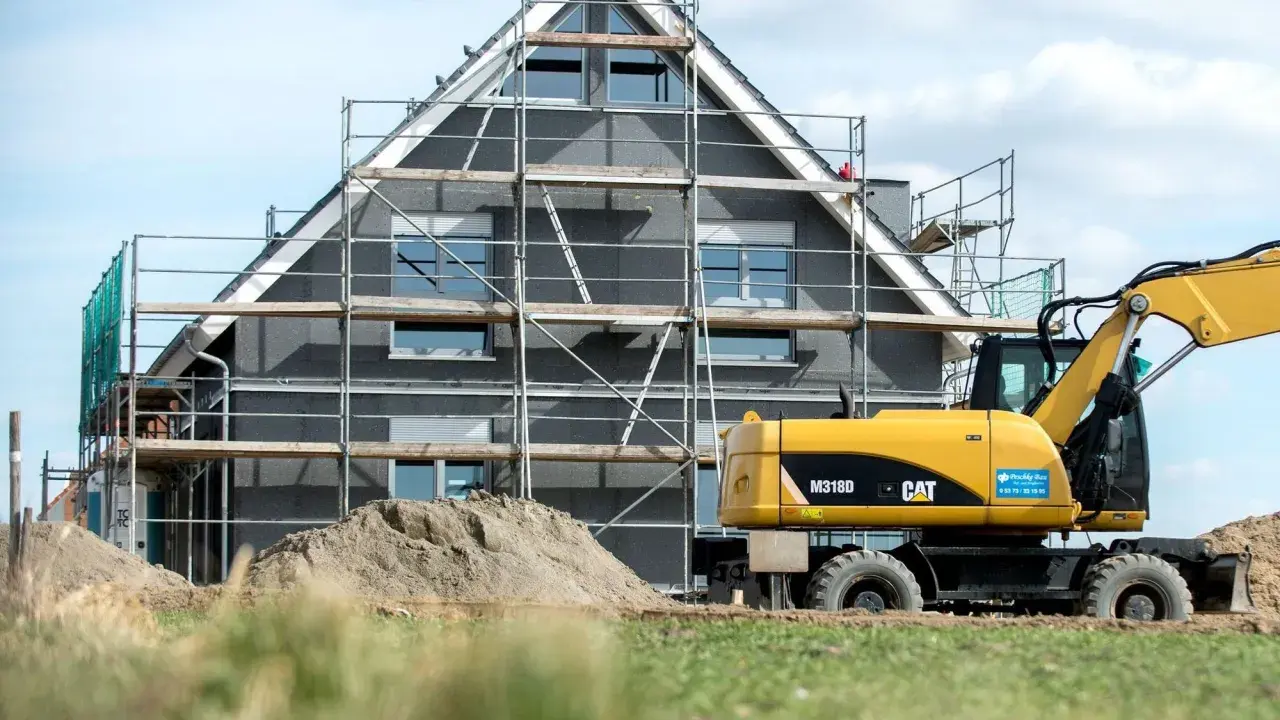 Ein Haus im Bau mit Gerüst und einem Bagger. Die bauseitigen Leistungen sind im vollen Gange.
