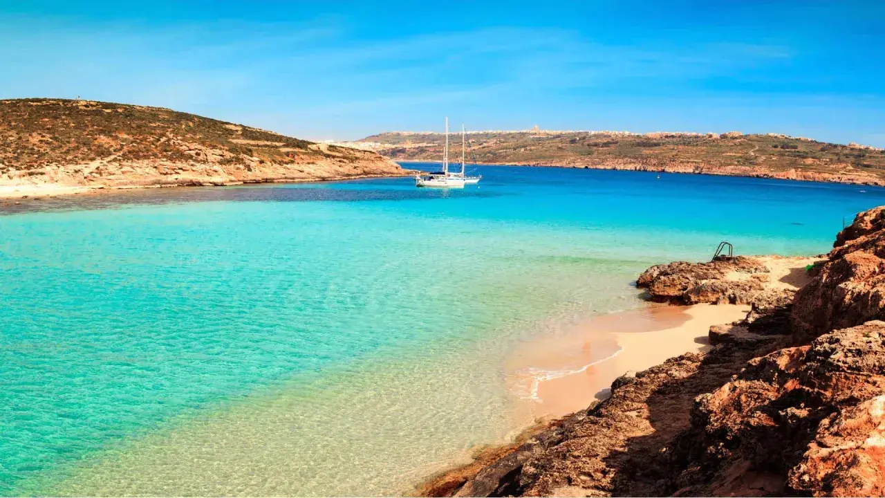 Traumhafter Malta Strand mit türkisfarbenem Wasser, einer einsamen Bucht und einem Segelboot. Perfekt für einen entspannten Urlaub.