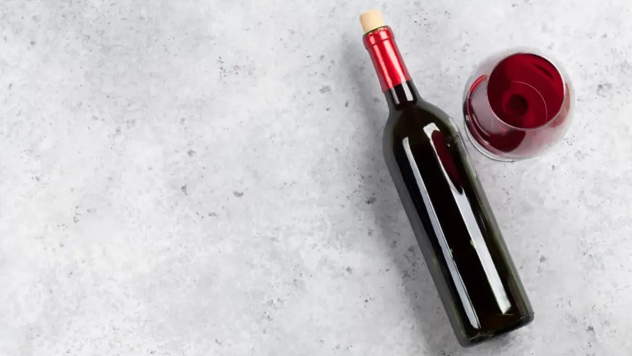 En flaska tamaral vin och ett glas rött vin på ett grått, stenig bakgrund.