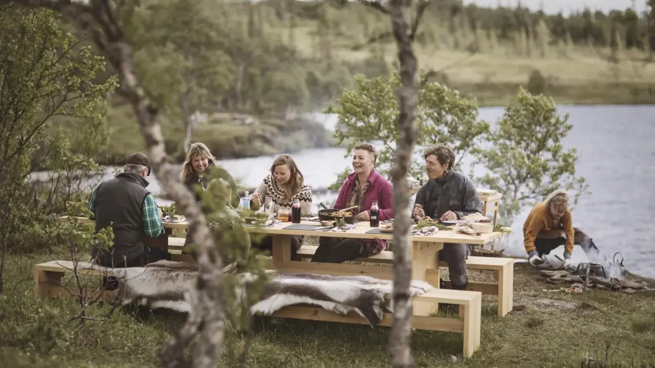 Vänner njuter av en måltid vid en sjö, en hyllning till det ätbara landet Sverige.
